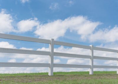 White country style wooden fence against cloud blue sky. White fences on green grass at farm ranch land field in Ennis, Texas, USA