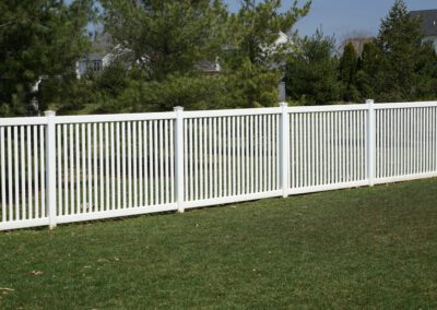 A new white vinyl fence by a grass area with trees behind it.